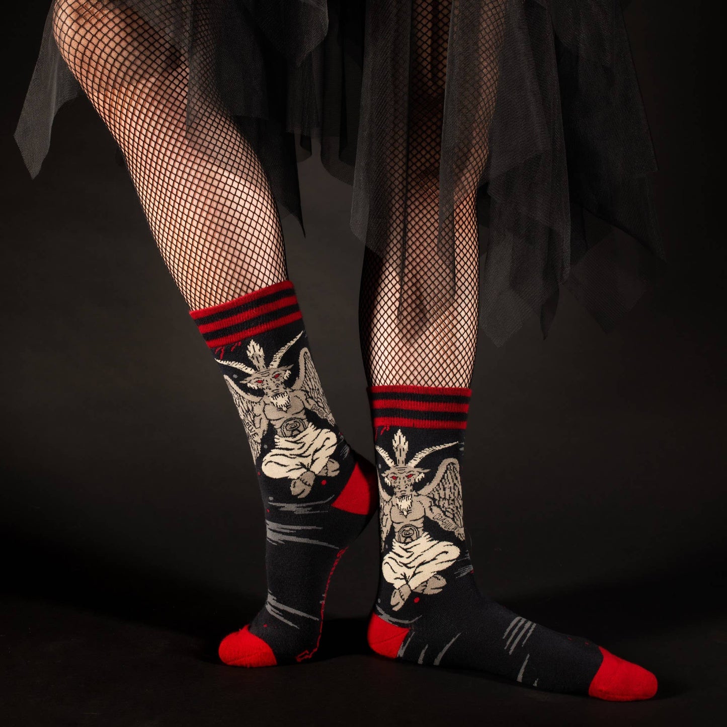 Model wearing a pair of socks featuring baphomet. Black legs, red heel, toe and cuff.