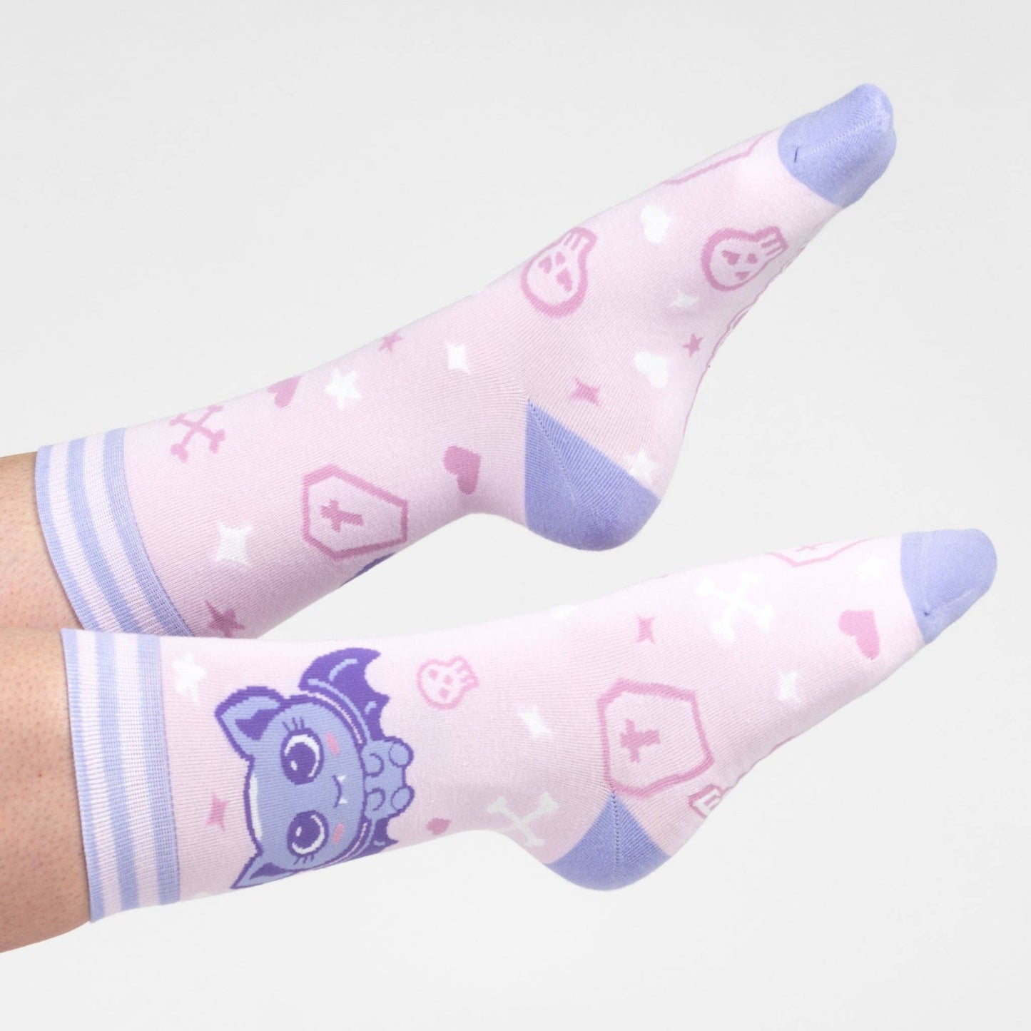 A model wearing a pair of socks with a cute bat motif. Pink legs, light purple heel, toe and cuff.