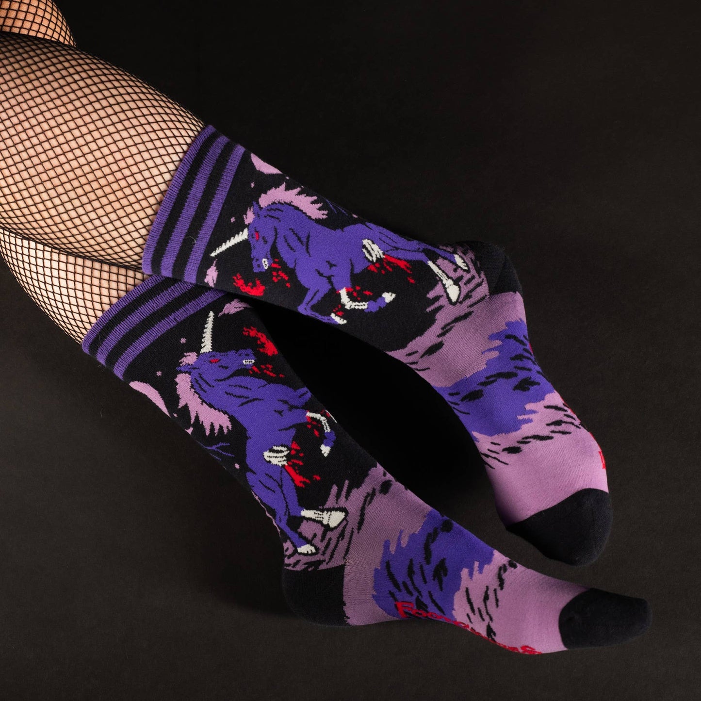 Model wearing a pair of socks with a dark and twisted unicron motif. Pink and purple legs, black heel, toe and cuff.