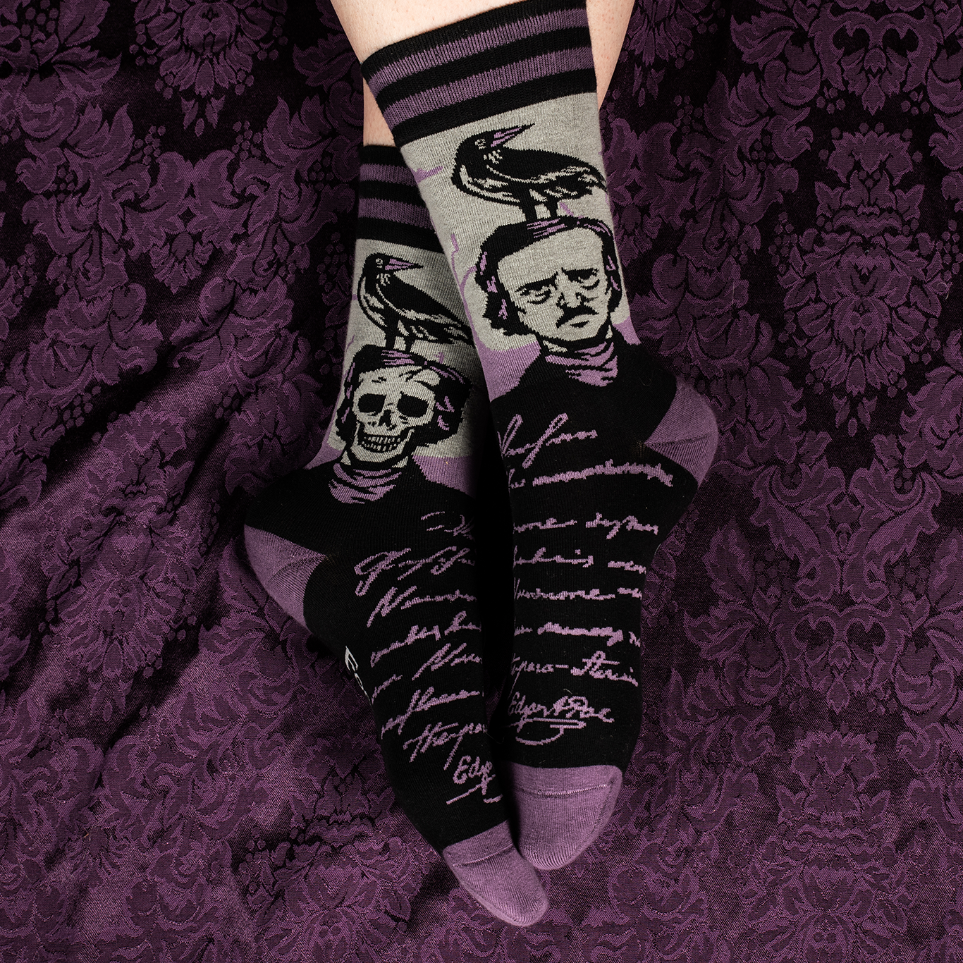 A pair of socks depicting a skeleton Edgar Allan Poe with a raven. Purple toes, heel and cuff.
