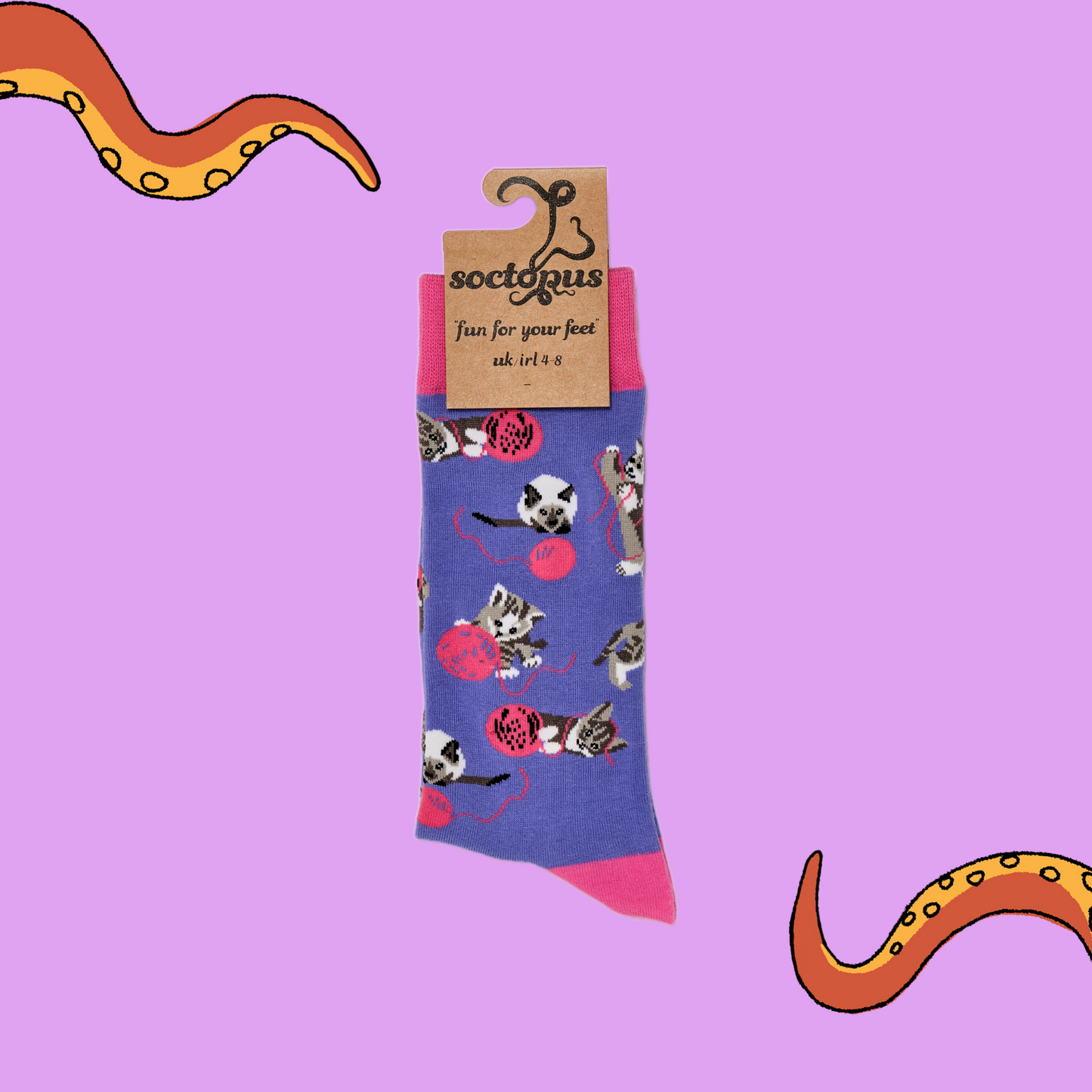 A pair of socks depicting cats playing with wool. Purple legs, pink cuff, heel and toe. In Soctopus Packaging.