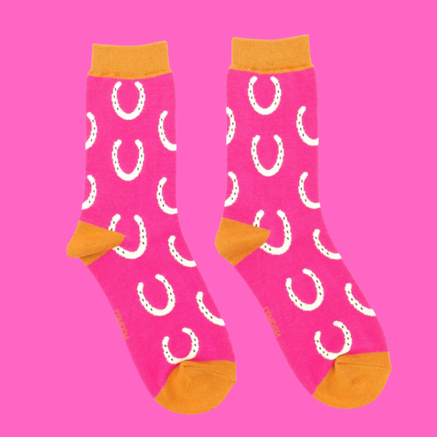 Horseshoes Bamboo Socks - Miss Sparrow. A pair of bright pink socks featuring a white horseshoe pattern. Orange cuffs, heels, and toes. Socks shown on a pink background.