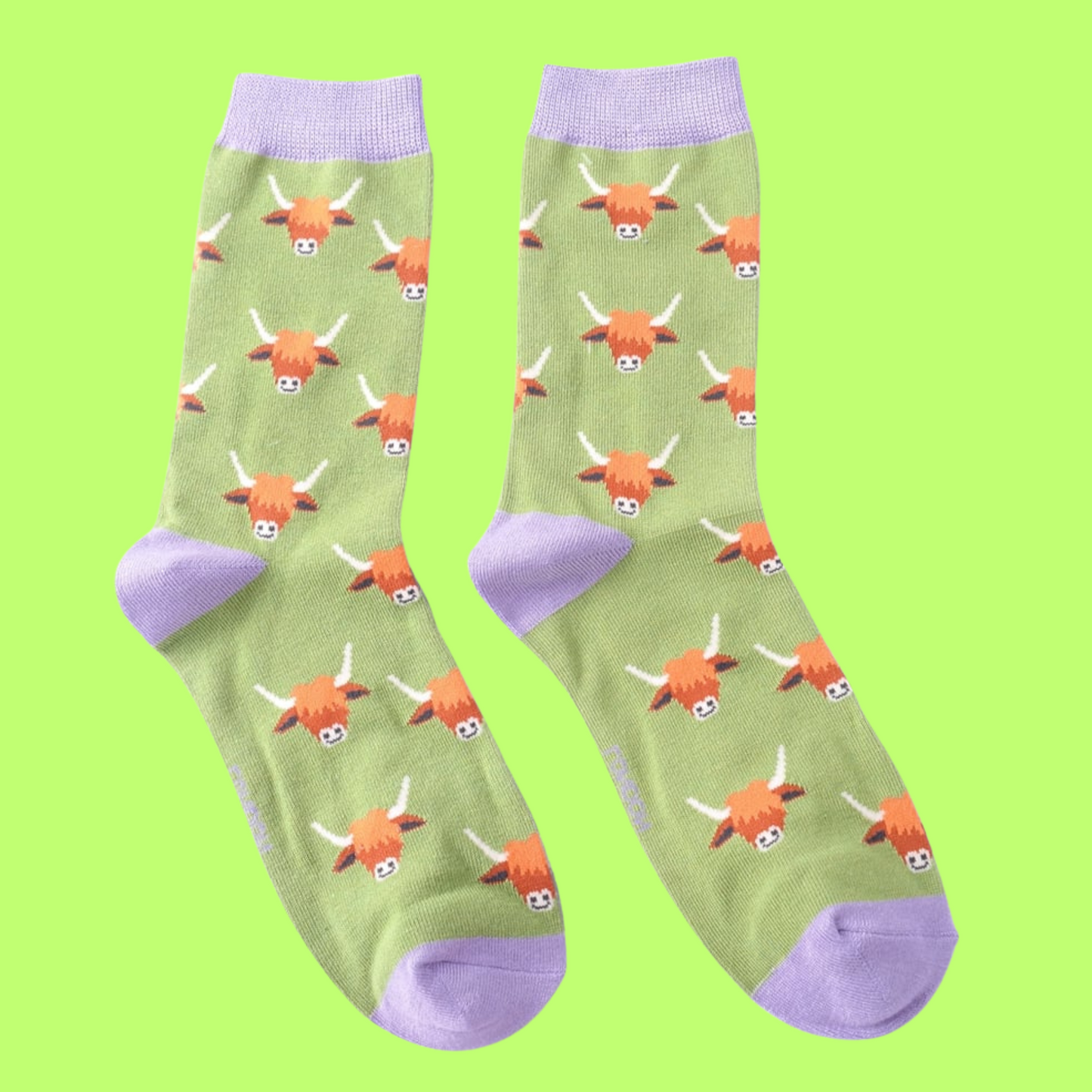 A pair of socks featuring a highland cow motif. Green legs, purple heel, toe and cuff.