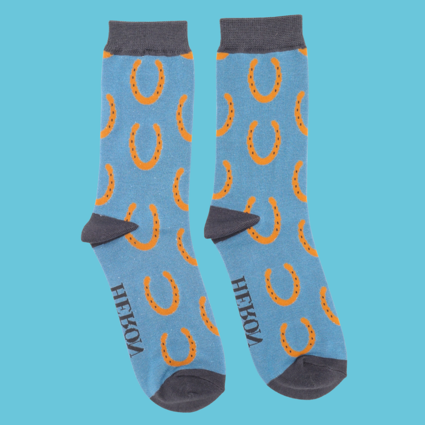 Horseshoes Bamboo Socks - Miss Sparrow. A pair of blue socks featuring an orange horseshoe pattern. Grey cuffs, heels, and toes. Socks shown on a blue background.