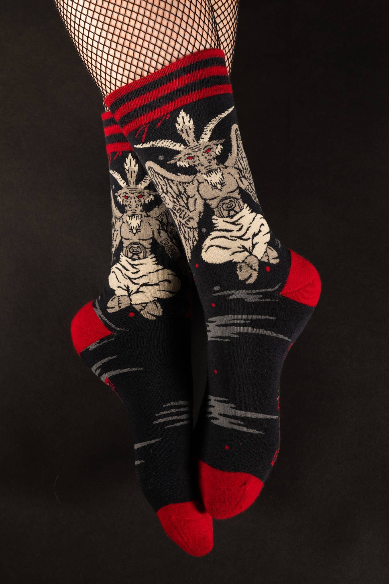 Model wearing a pair of socks featuring baphomet. Black legs, red heel, toe and cuff.