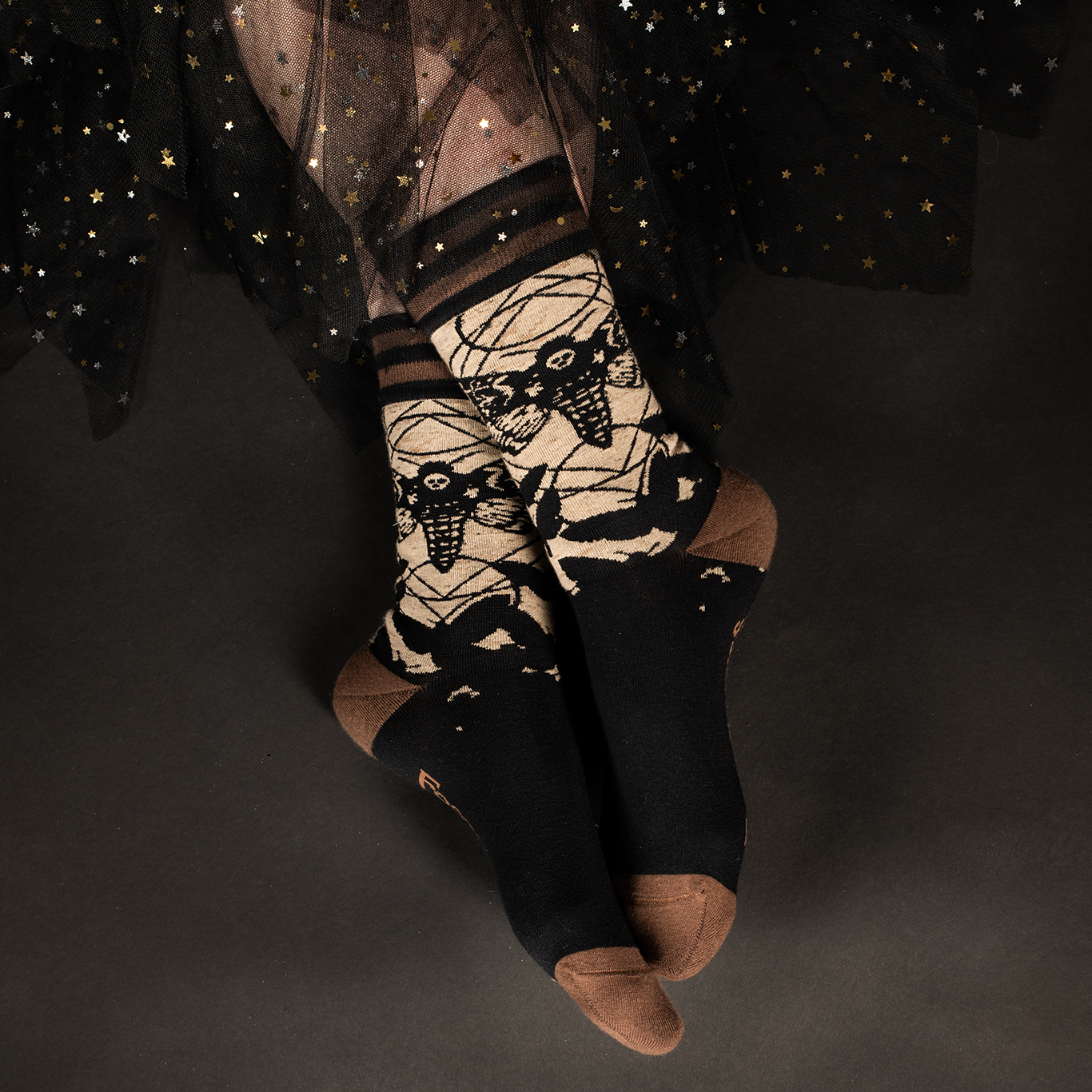 A model wearing a pair of socks depicting a deaths head moth. Brown toes, heel and cuff.