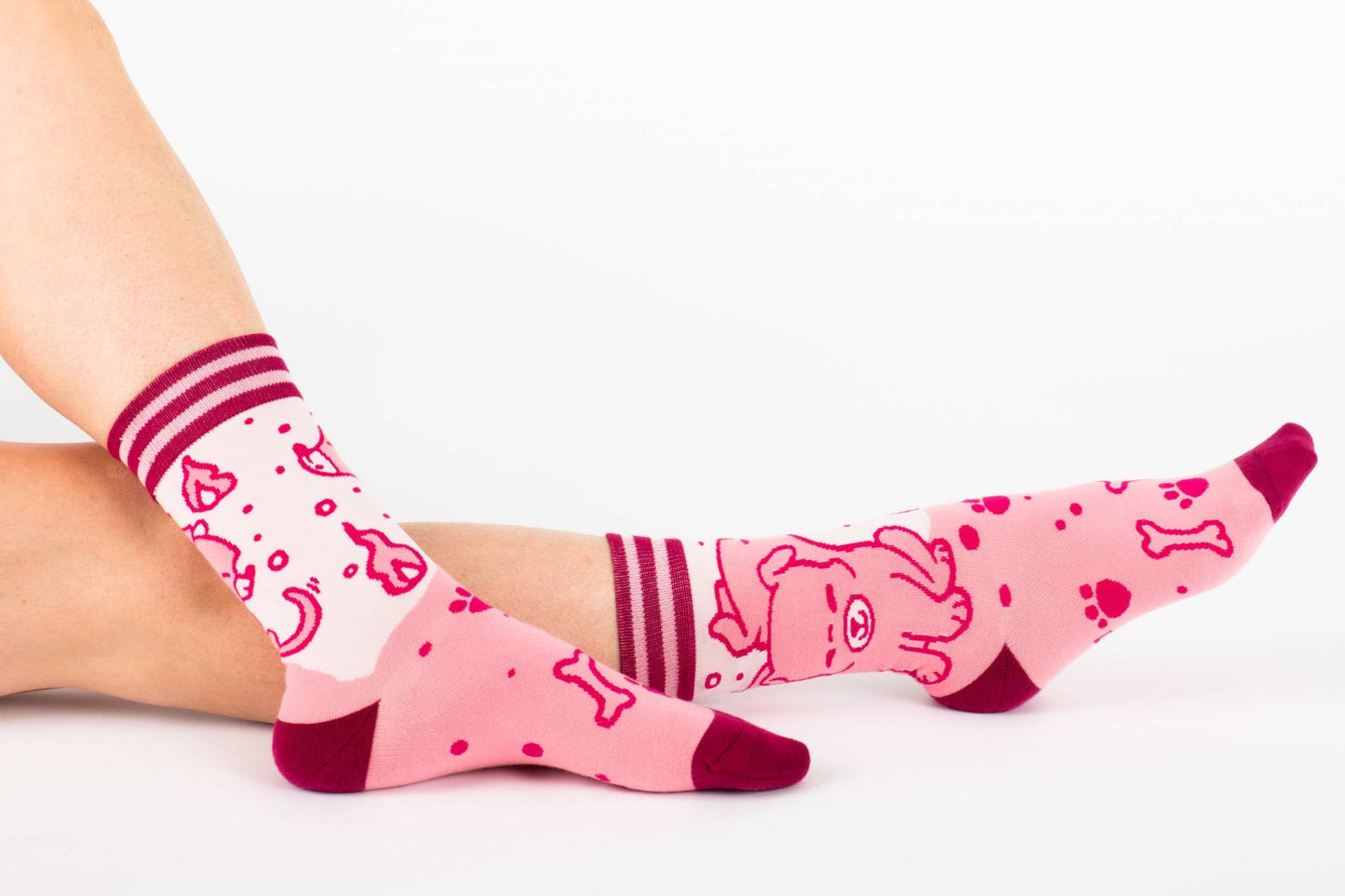 A model wearing a pair of socks featuring a cute 3 headed dog. Pink legs, dark pink heel, toe and cuff.
