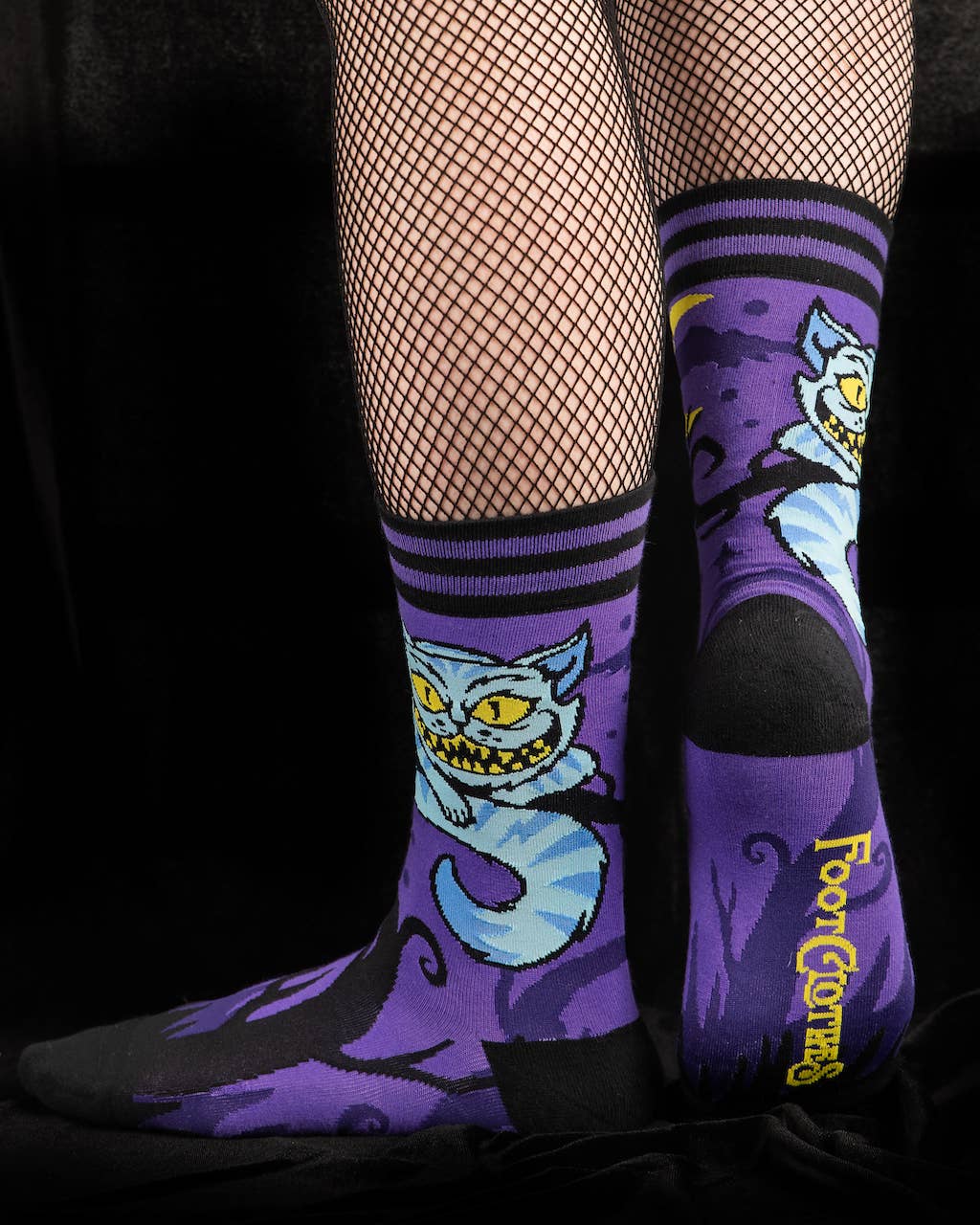 A model wearing a pair of socks featuring the cheshire cat. Purple legs, black heel, cuff and toe.