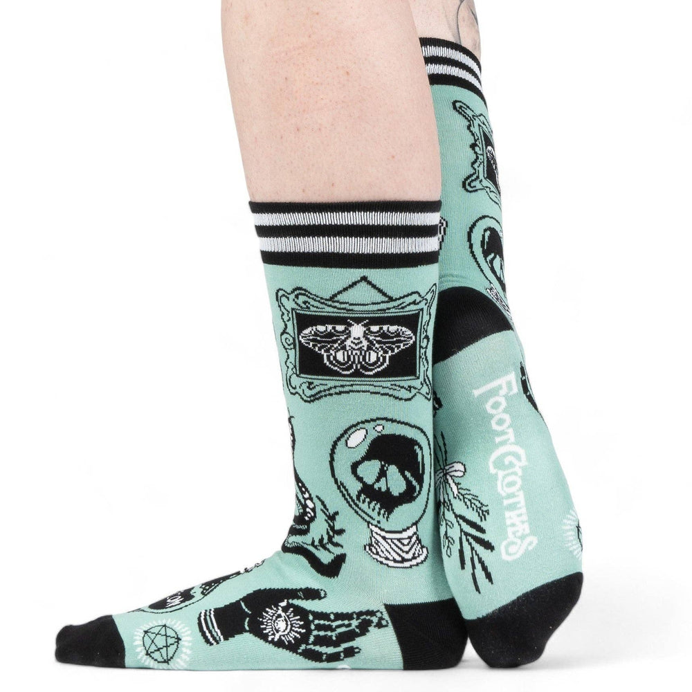 
                      
                        A model wearing a pair of socks featuring occult and magic symbols. Green legs, black, heel and toe. 
                      
                    