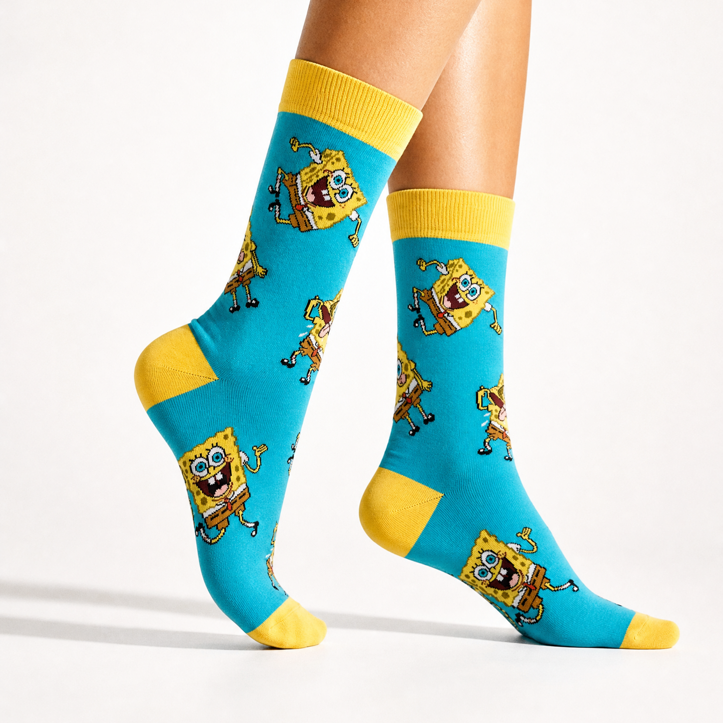 A pair of crew socks with a bright turquoise blue background and yellow cuffs, heels, and toes, featuring a repeating spongebob pattern, shown on a model's legs against a white studio background.