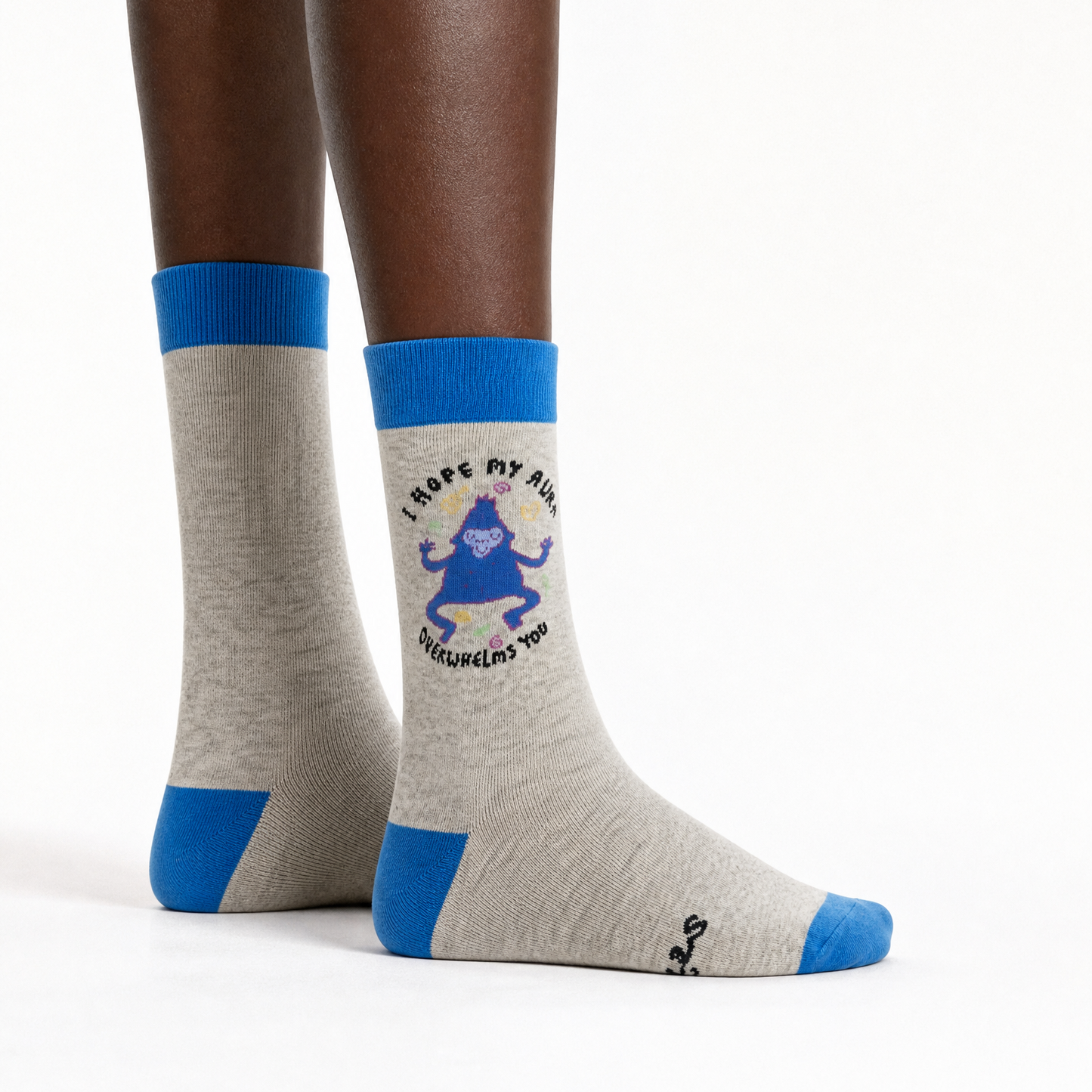 A pair of crew socks worn on a person's feet, shown against a plain white studio background. The socks are heather light grey with bright blue cuffs, heels, and toes, and the right sock features a blue cartoon character graphic. 