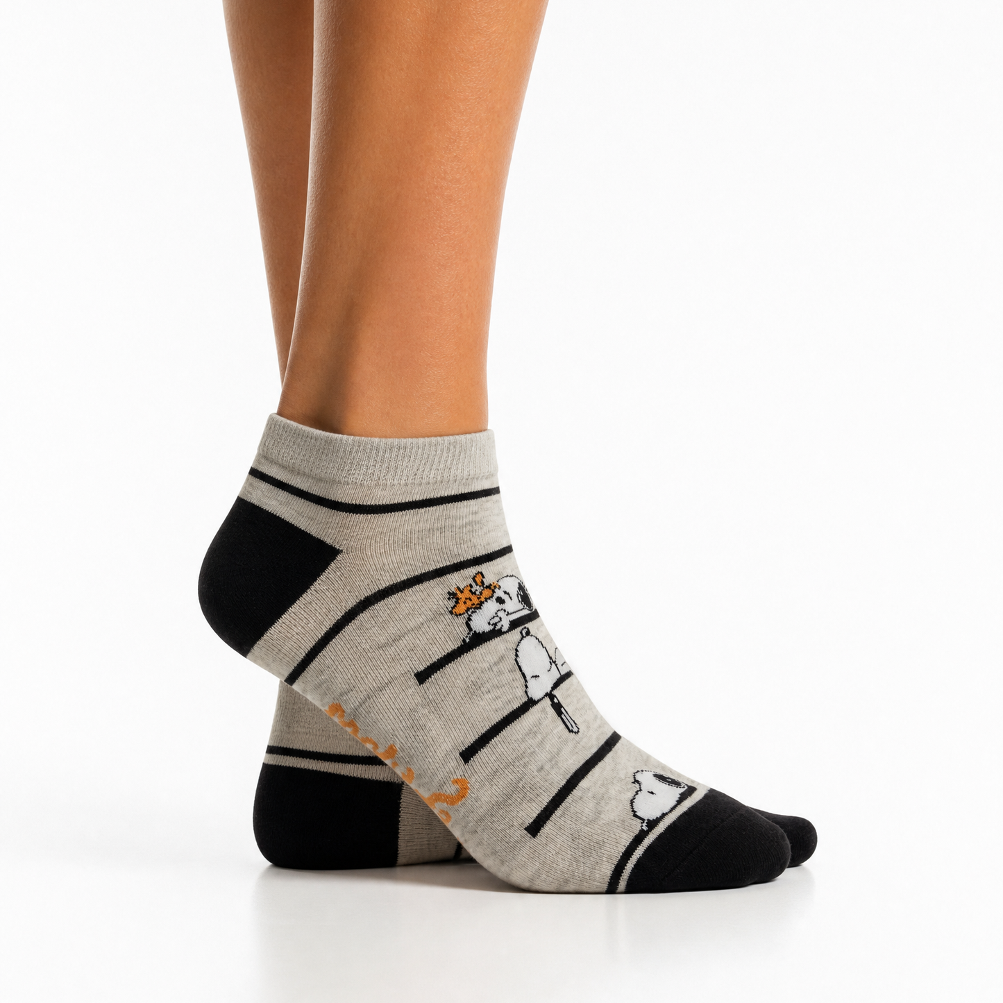 A pair of low-cut ankle socks worn on a person's feet, featuring a light grey and black striped pattern snoopy illustrations and orange stitching along the sole.