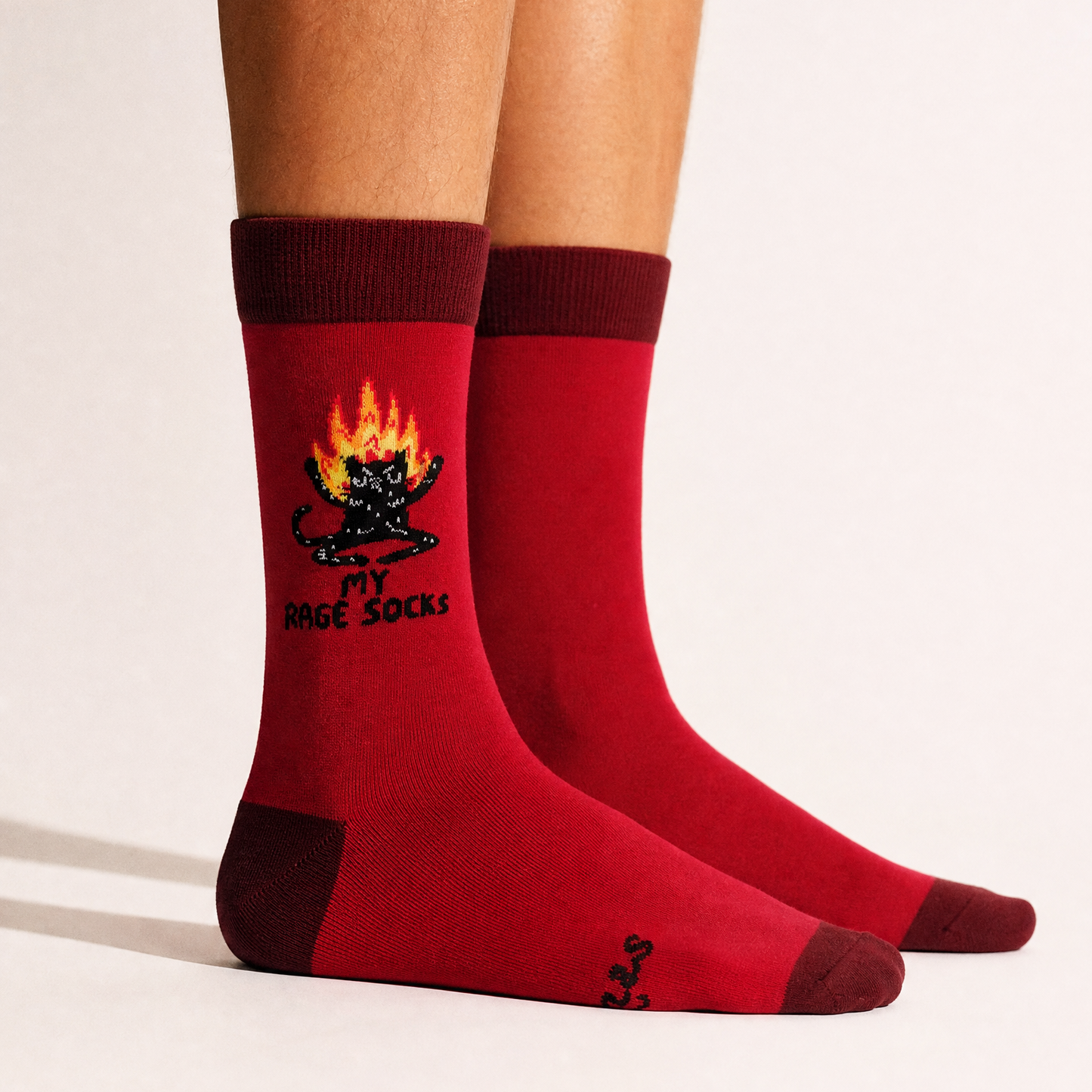 Red crew socks worn on a person's feet, featuring a black cat with orange flames and the text 'My Rage Socks' on the front sock.