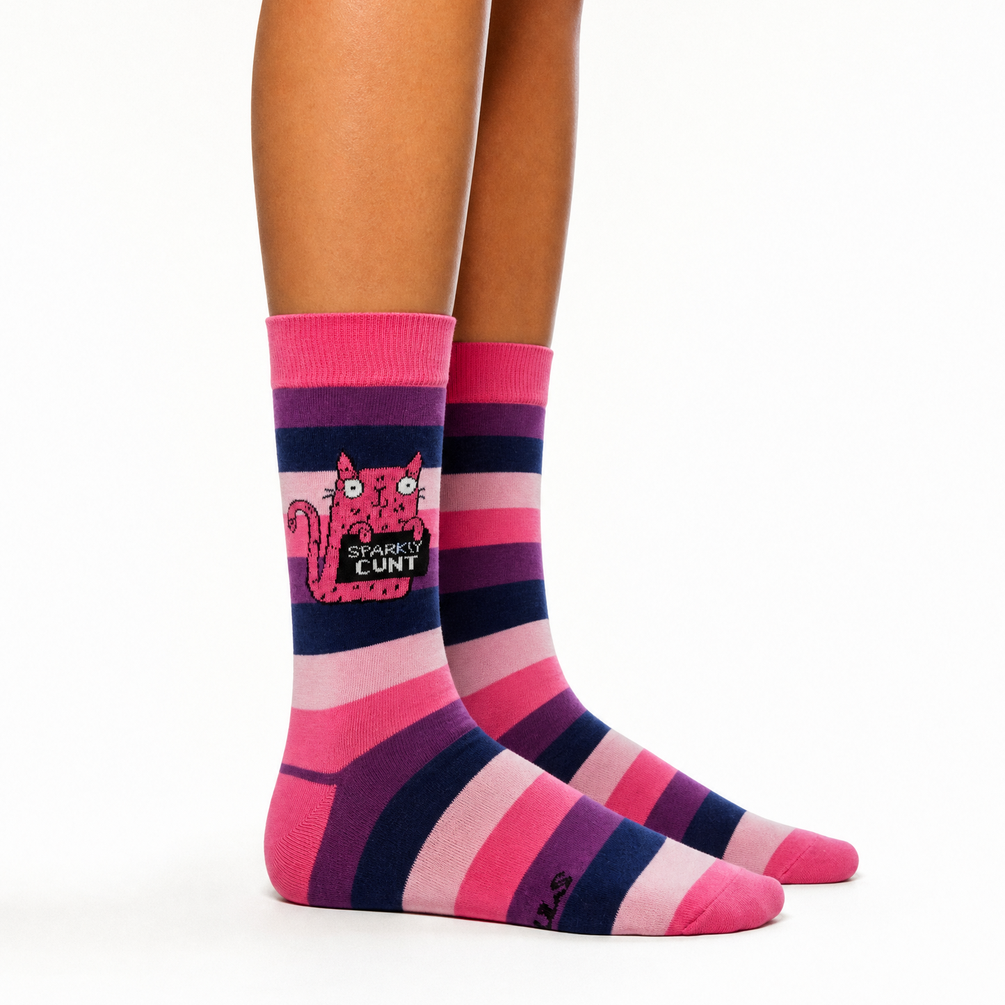 A pair of crew socks worn on a person's legs, featuring horizontal stripes in pink, purple, and light pink, with a cartoon cat graphic and the text 'SPARKLY CUNT' on the front sock.