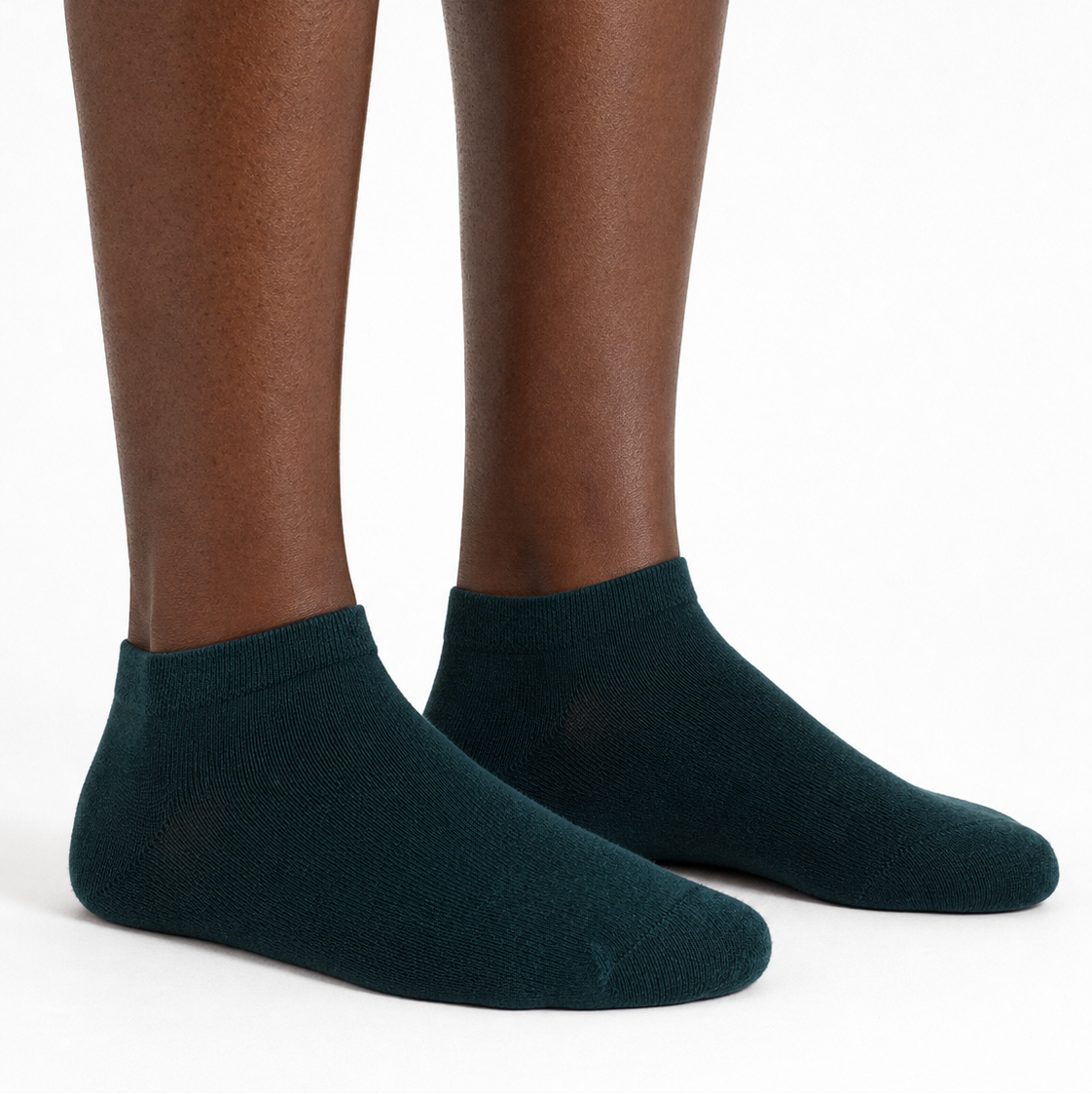 A close-up of a person's feet wearing dark teal green low-cut socks against a plain white background.