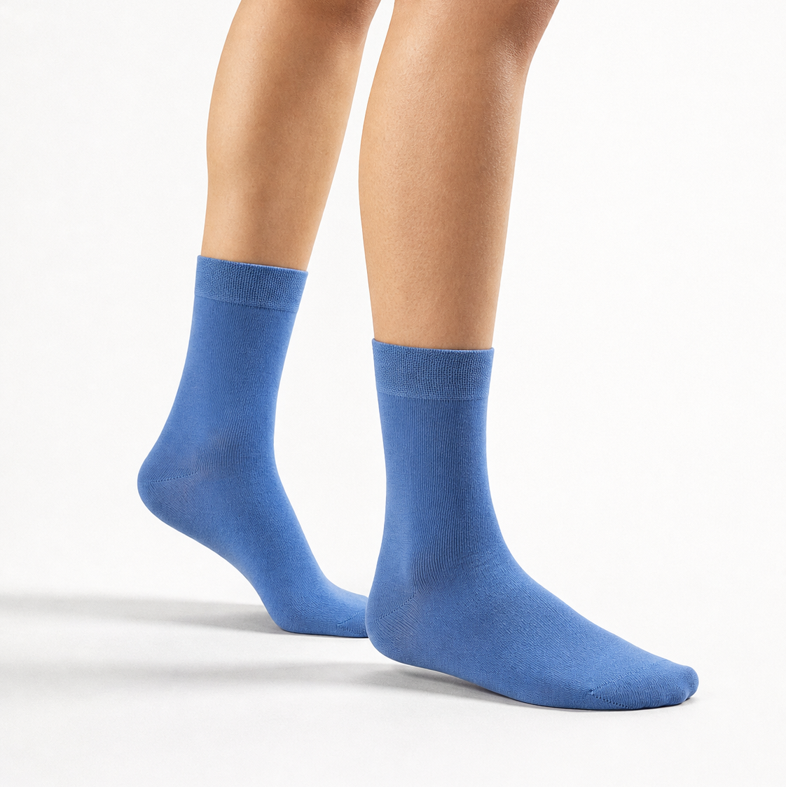 A pair of medium blue crew socks worn on a model's feet, shown against a clean white studio background.
