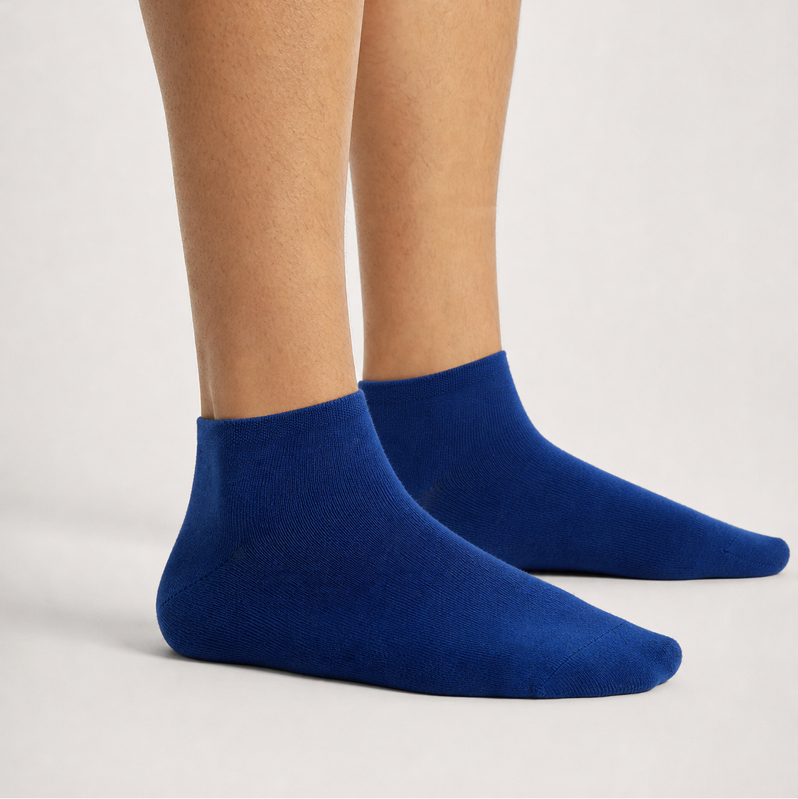 A pair of solid royal blue low-cut ankle socks worn on a person's feet, shown against a clean, light gray studio background.