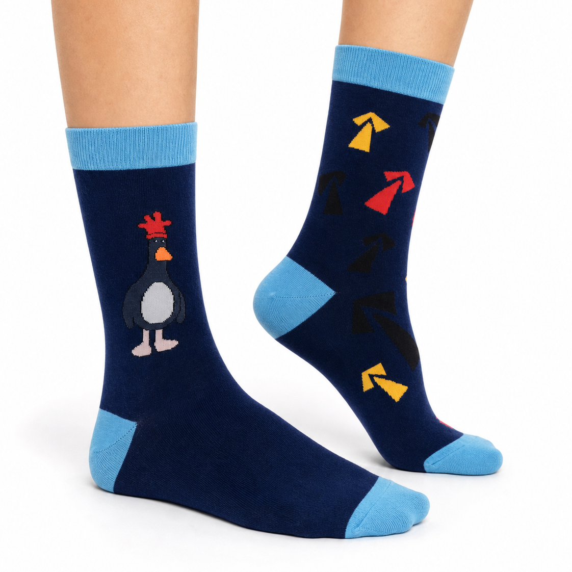 A pair of navy blue crew socks with light blue cuffs, heels, and toes, featuring a cartoon penguin on one sock and colorful arrow graphics on the other, shown on a person's feet against a white background.