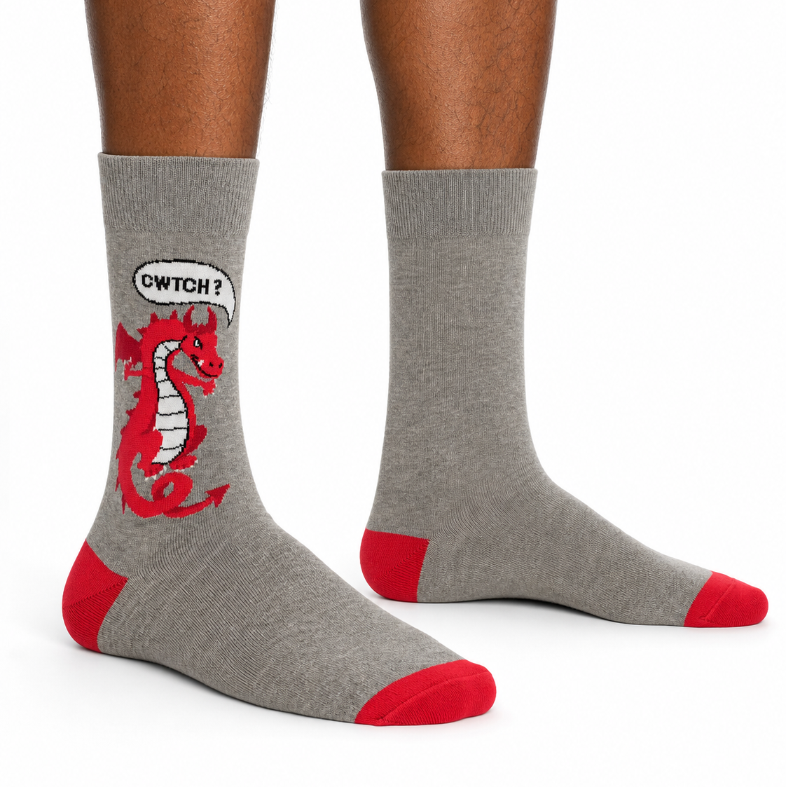 Gray crew socks with red toe and heel accents, featuring a red cartoon dragon graphic with a speech bubble that says 'CWTCH?' on one sock, shown on a model's feet against a white background.