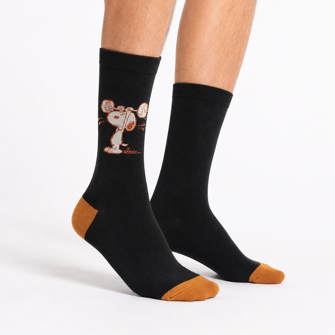 A pair of black crew socks with tan toes and heels, featuring a cartoon graphic of Snoopy and Wally on one sock, shown on a model's feet against a white background.