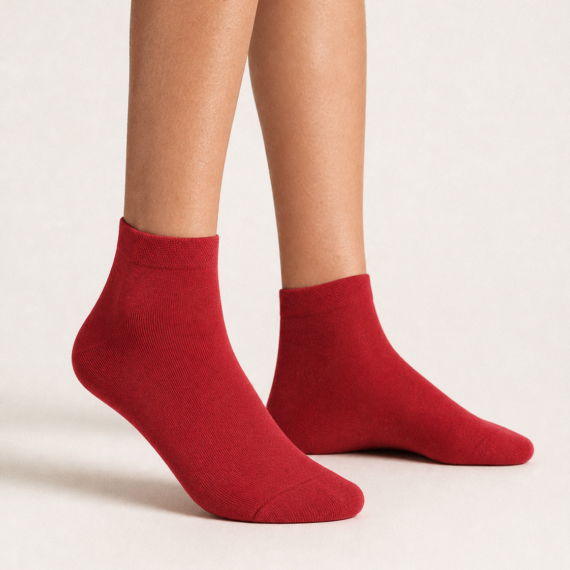 A pair of red ankle socks worn on a model's feet, shown against a clean, light beige studio background.