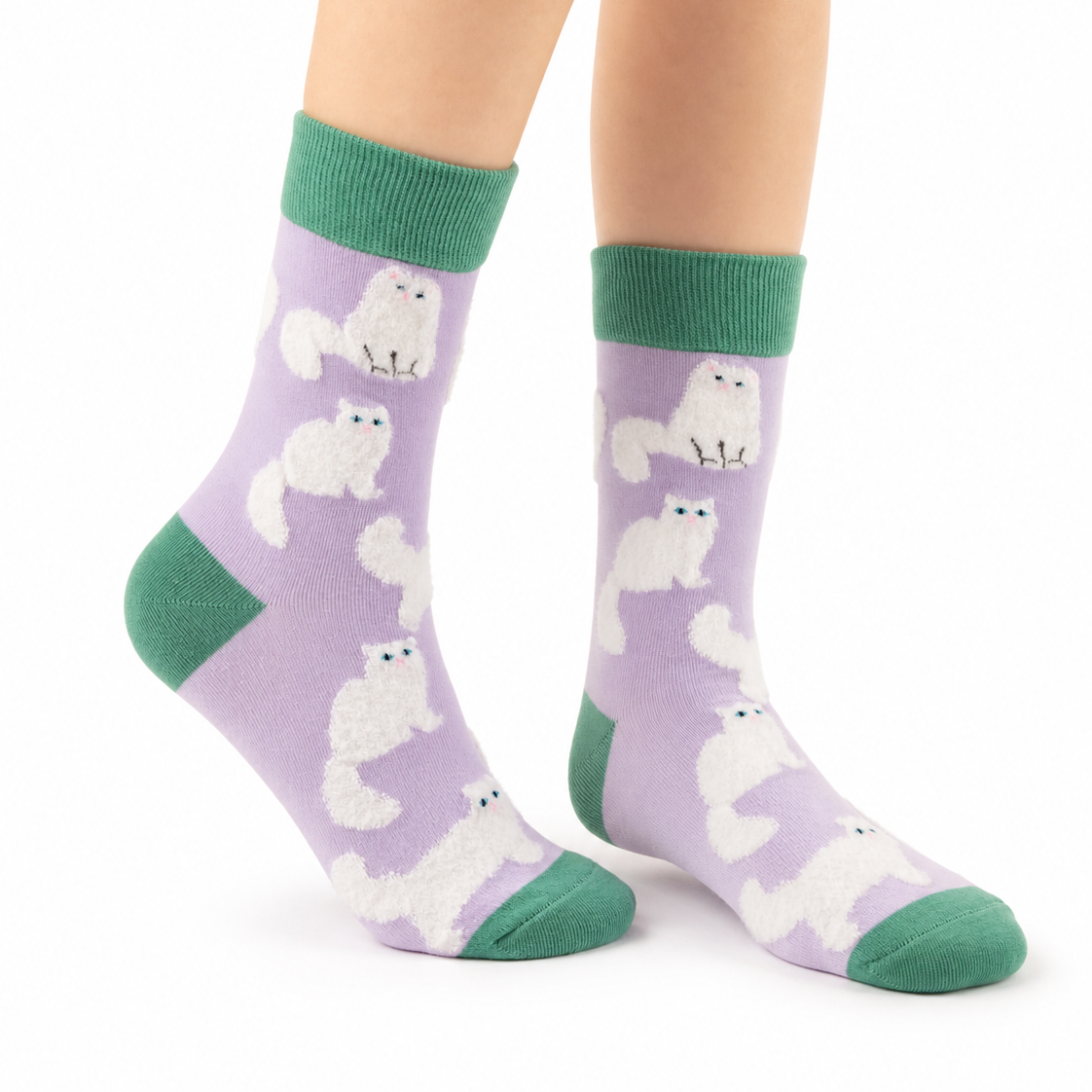 A pair of crew socks worn on a person's feet, featuring a light purple background with a repeating pattern of white fluffy cats and solid green cuffs, heels, and toes, shown against a plain white background.