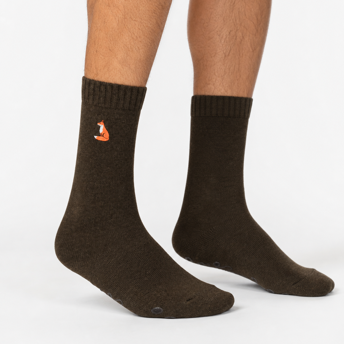 A pair of dark brown crew socks worn on a person's feet, featuring a small orange fox logo on the left sock, set against a plain light gray background.