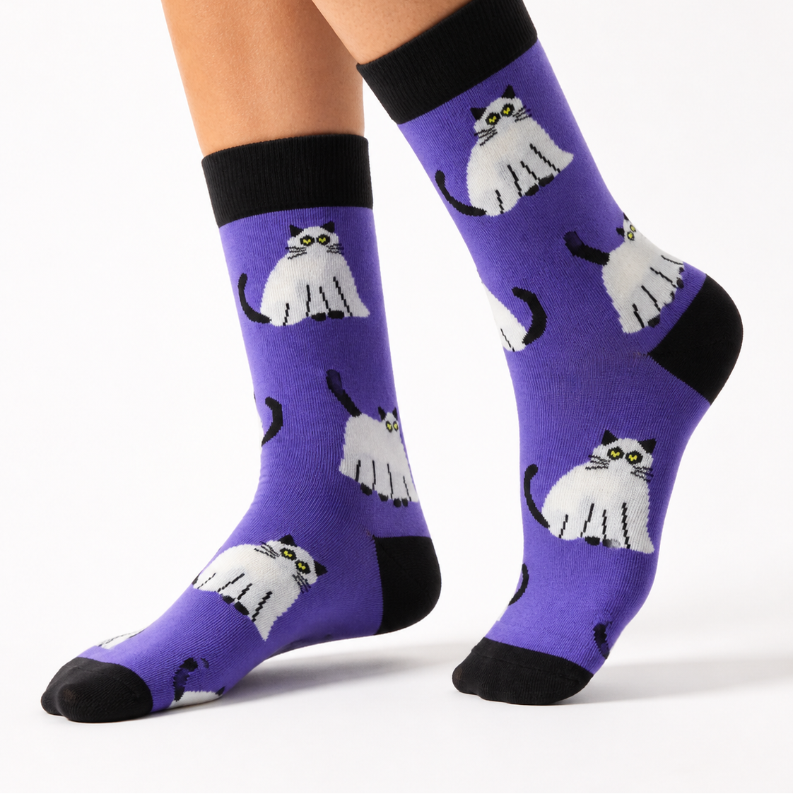 Purple crew socks with a repeating pattern of white cats with black outlines, worn on a person's legs against a plain white background.