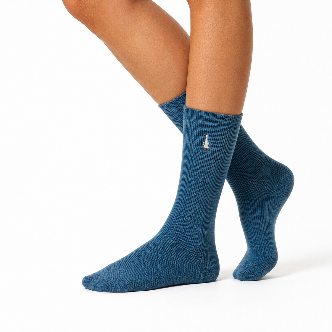 A close-up of a person's legs and feet wearing a pair of ribbed crew socks in a muted blue color, with a small white embroidered rabbit logo on the side of each sock, against a plain white background.