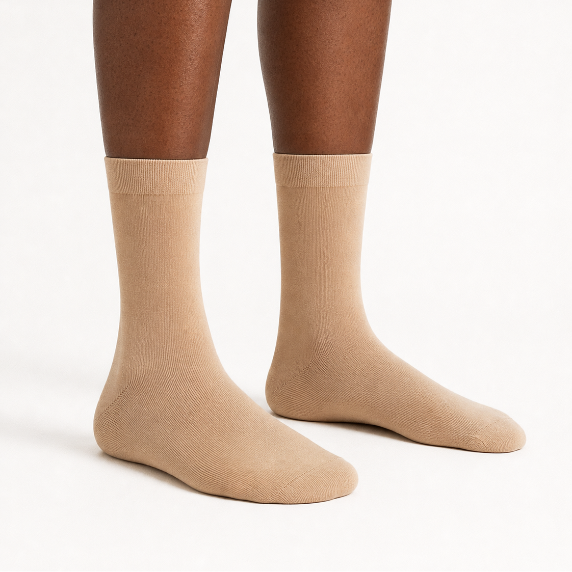 A pair of crew socks in a solid tan color, shown on a model's feet against a clean white studio background.