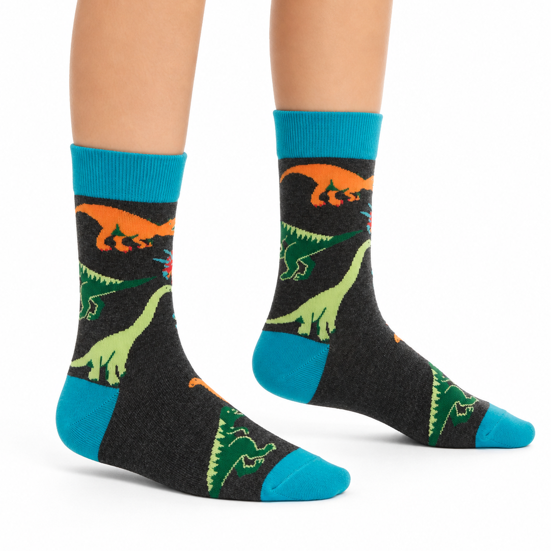 A pair of crew socks worn on a child's feet, featuring a black background with colorful dinosaur illustrations in green, orange, and blue.