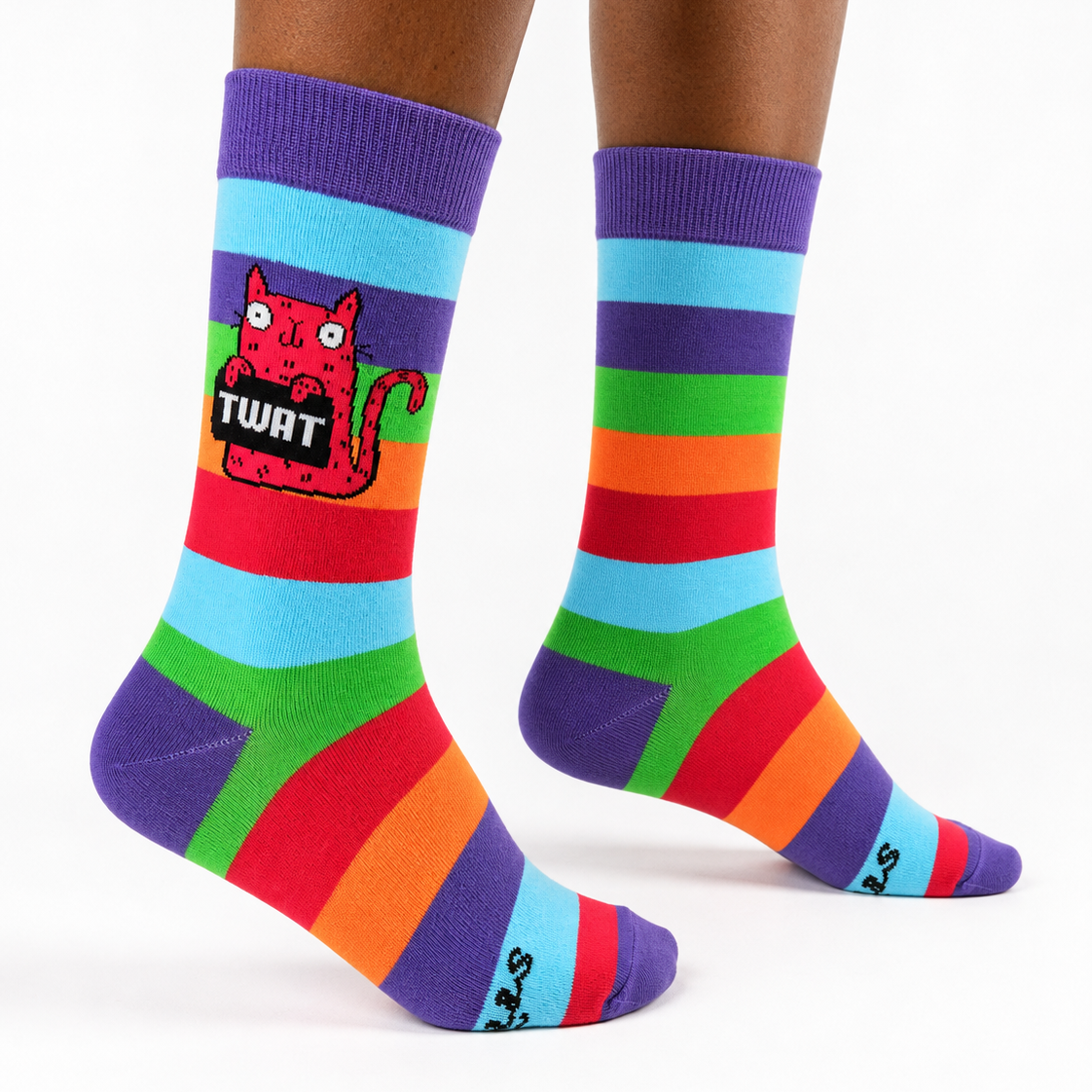 A pair of crew socks worn on a person's feet, featuring bold horizontal rainbow stripes in purple, blue, green, orange, and red, with a red cartoon cat graphic and the word 'TURT' on the left sock.