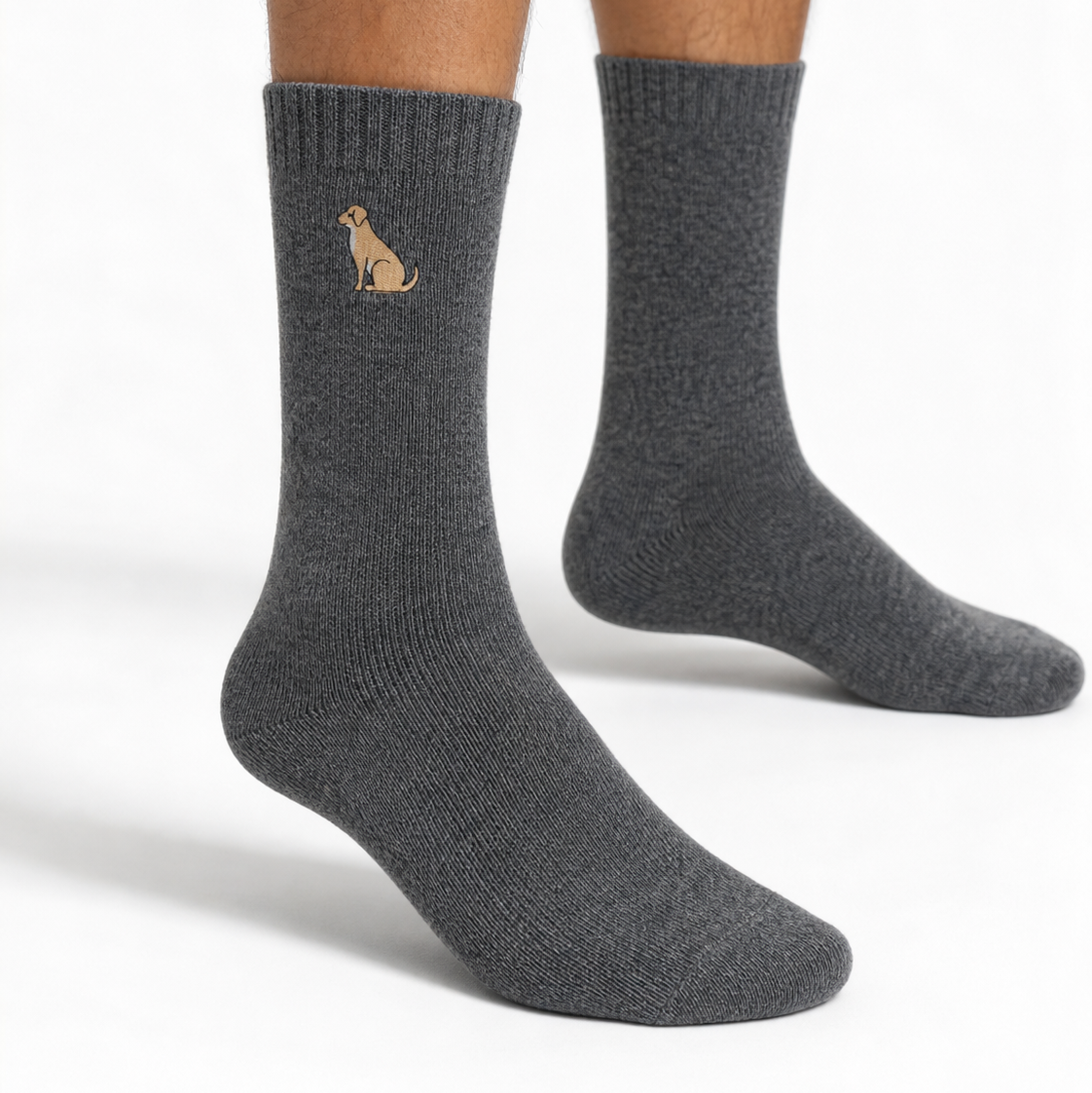 A pair of dark gray crew socks worn on a person's feet, featuring a small tan dog graphic on the front sock.