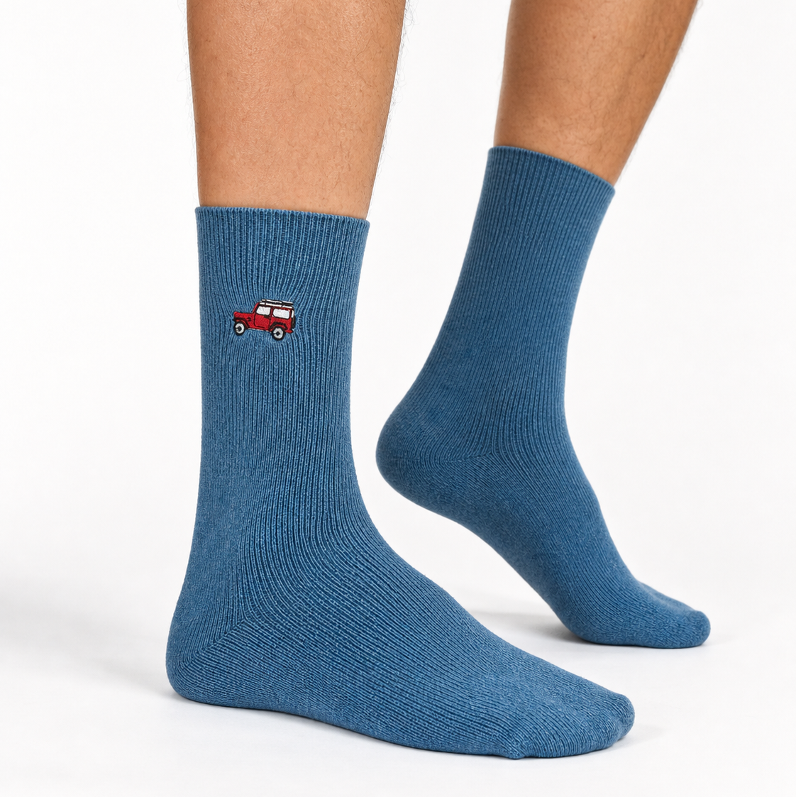 A pair of blue crew socks worn on a person's feet, featuring a small embroidered red and white truck graphic on the side of one sock, against a clean white background.