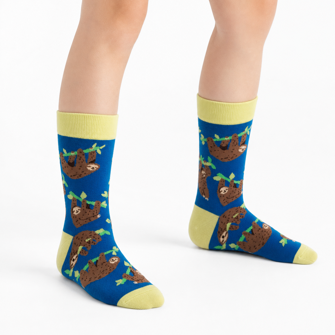 A person's feet and lower legs wearing blue crew socks with a repeating brown sloth pattern, yellow cuffs, heels, and toes, shown against a plain white studio background.