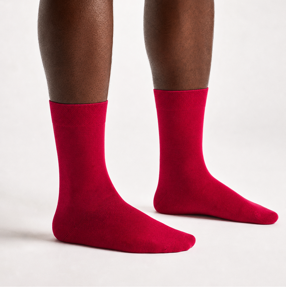 A close-up of a person's legs wearing bright red crew socks against a clean, light gray studio background.