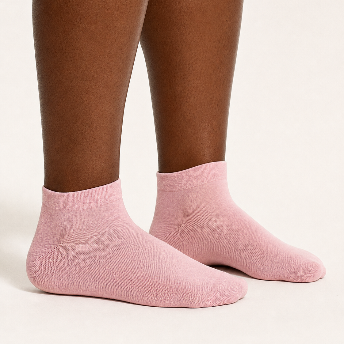 A close-up of a person's feet wearing light pink low-cut ankle socks against a plain off-white background.