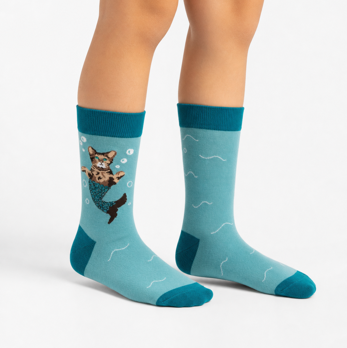 A person's legs wearing light blue crew socks with a mermaid cat graphic and teal accents, shown against a plain white studio background.