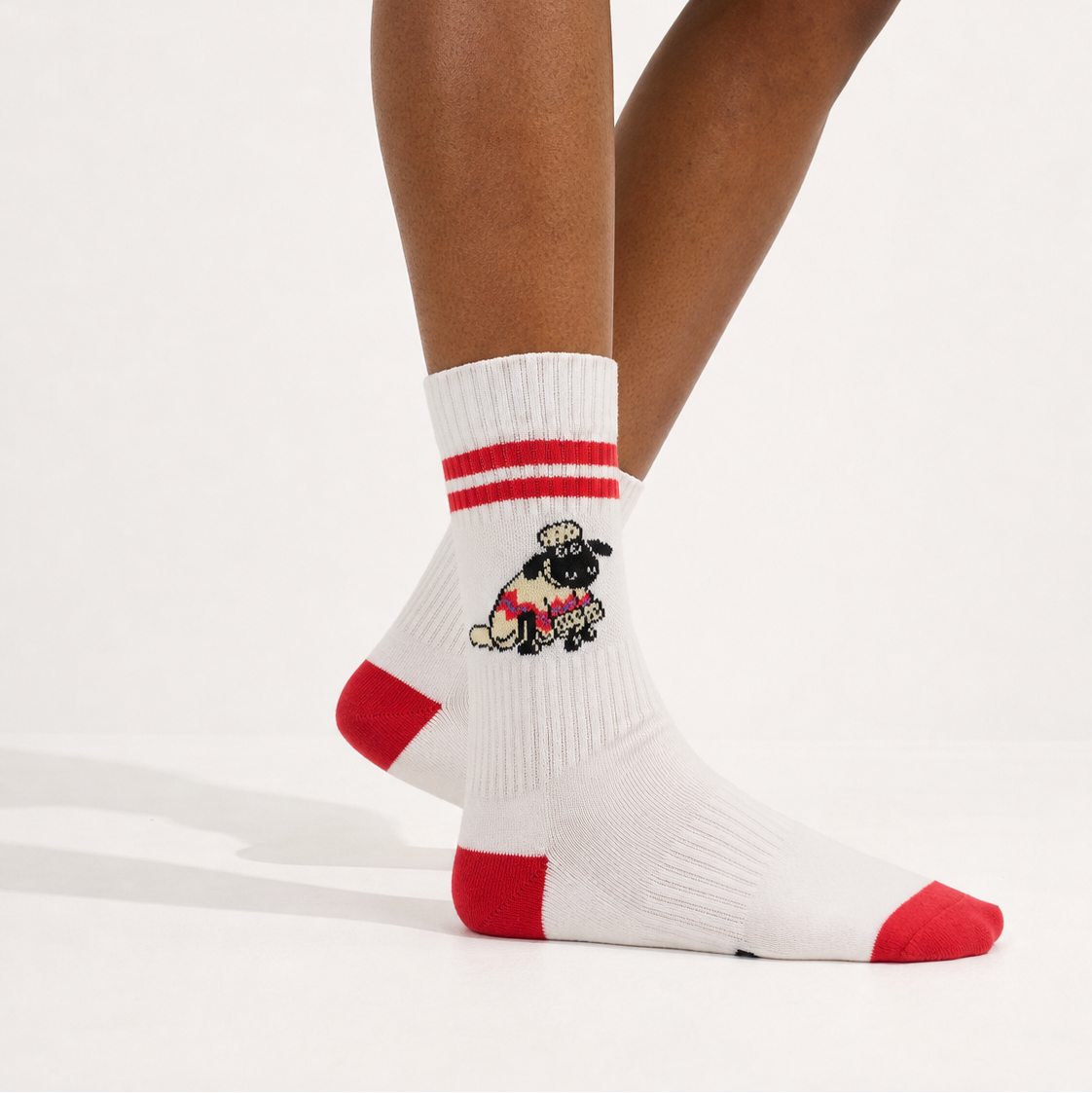 White crew socks with red toe, heel, and sole accents, featuring a small embroidered black-and-white dog character wearing a red sweater on the side. Shown on a model's feet against a clean white studio background.