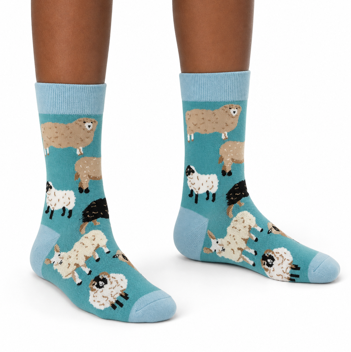 A pair of crew socks with a blue background and a pattern of cartoon sheep in beige, white, and black, shown on a person's feet against a white background.