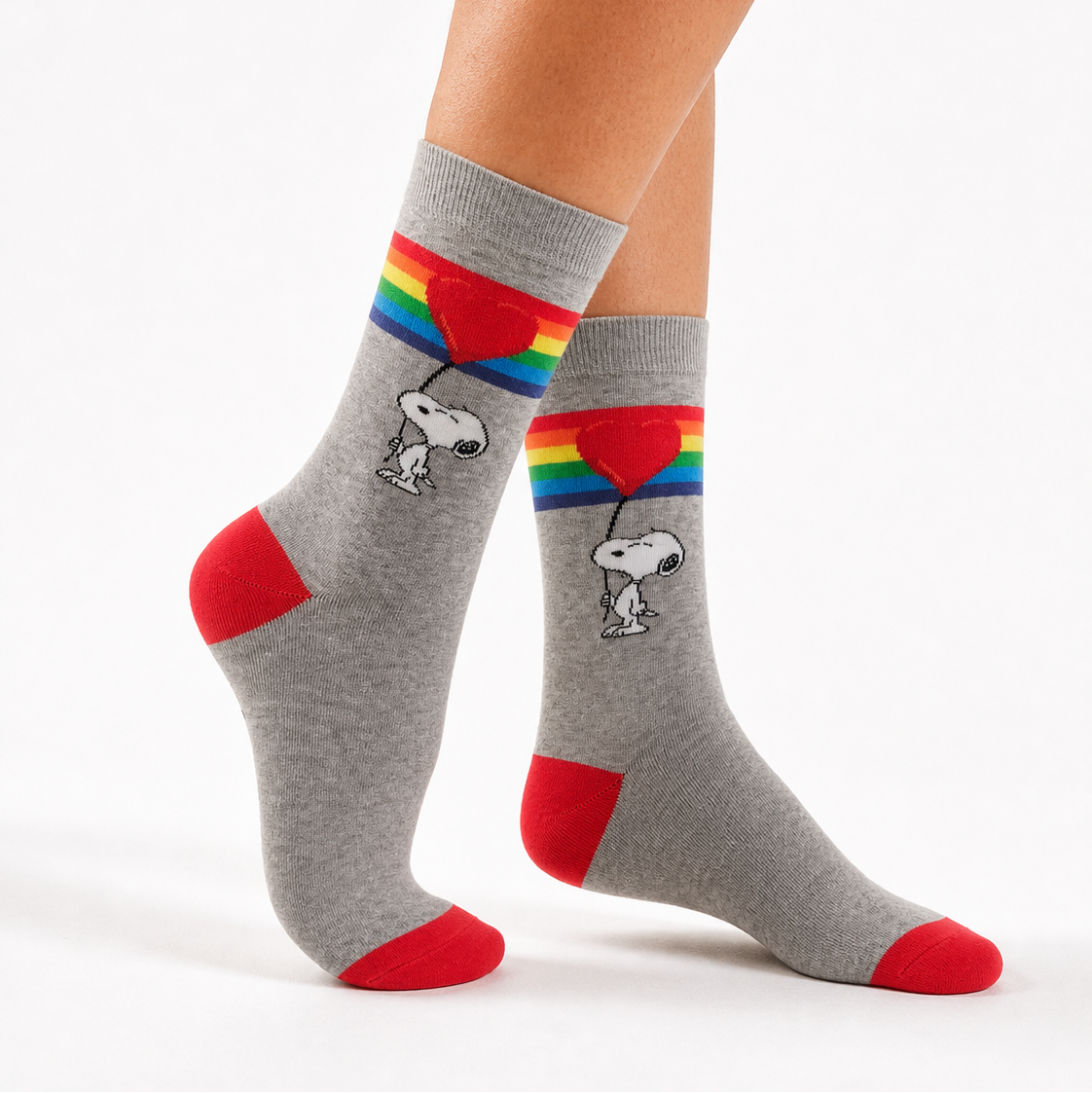 Gray crew socks with red heels, toes, and cuffs, featuring a printed graphic of Snoopy holding a rainbow balloon, shown on a model's feet against a white background.