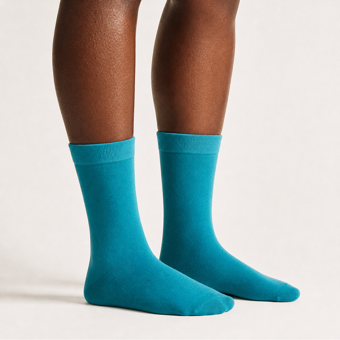 A pair of bright teal blue crew socks worn on a person's feet, shown from the calves down against a clean, light off-white studio background.