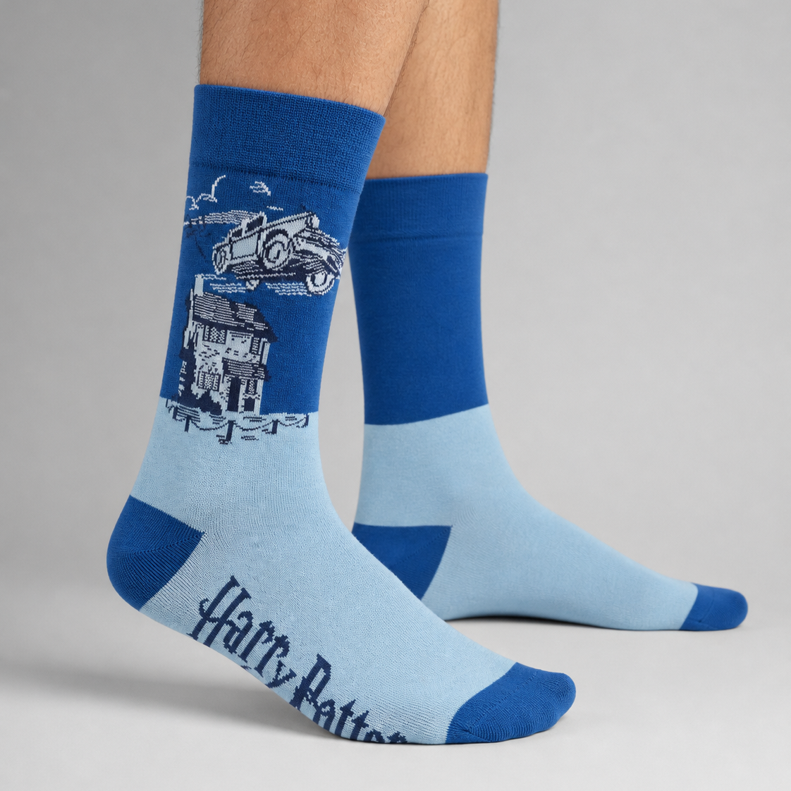 A pair of light blue and royal blue crew socks with a Harry Potter graphic and 'Harry Potter' text, shown on a person's feet against a neutral grey background.