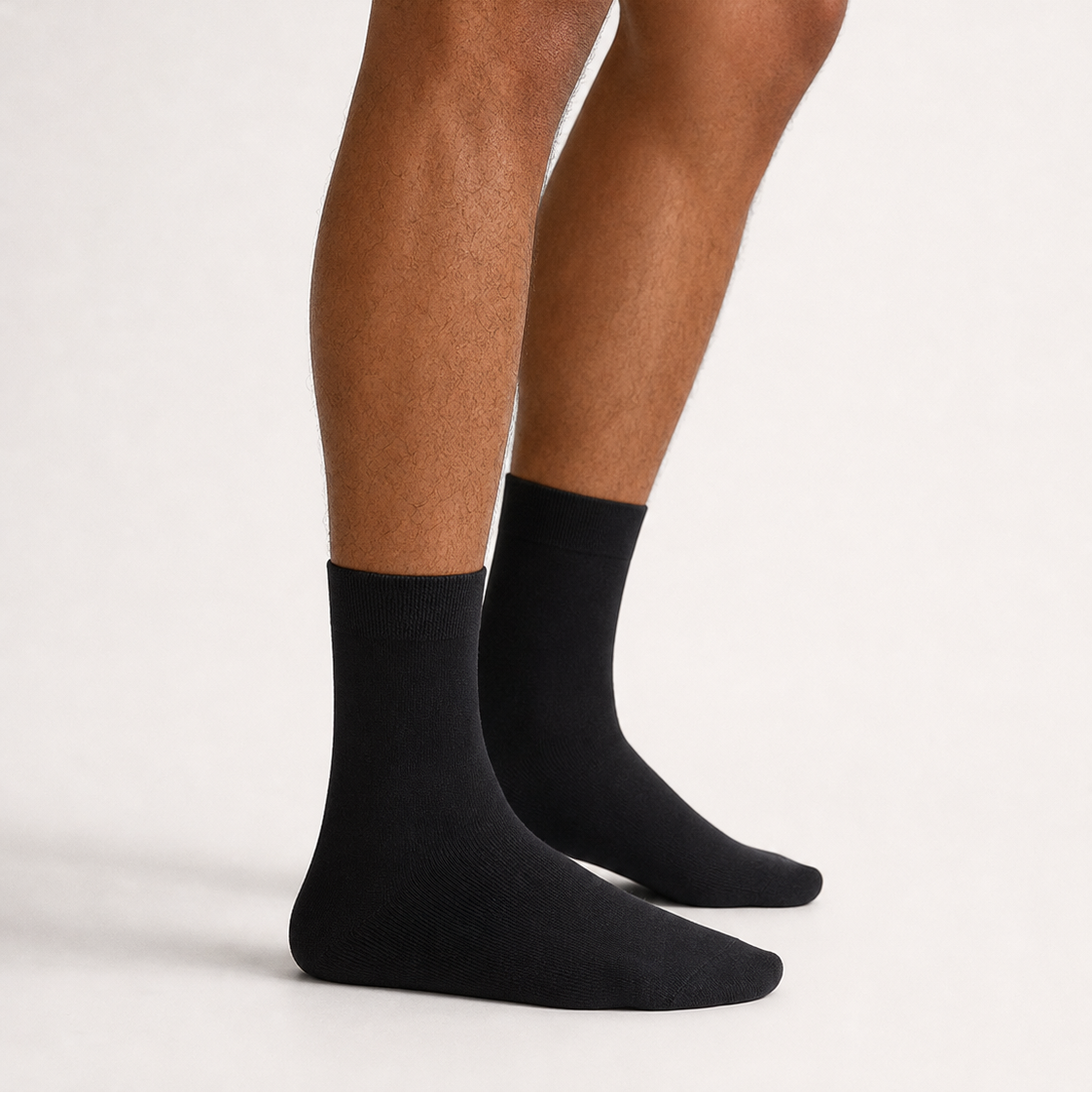 A close-up of a person's legs wearing a pair of plain black crew socks against a clean, light off-white studio background.