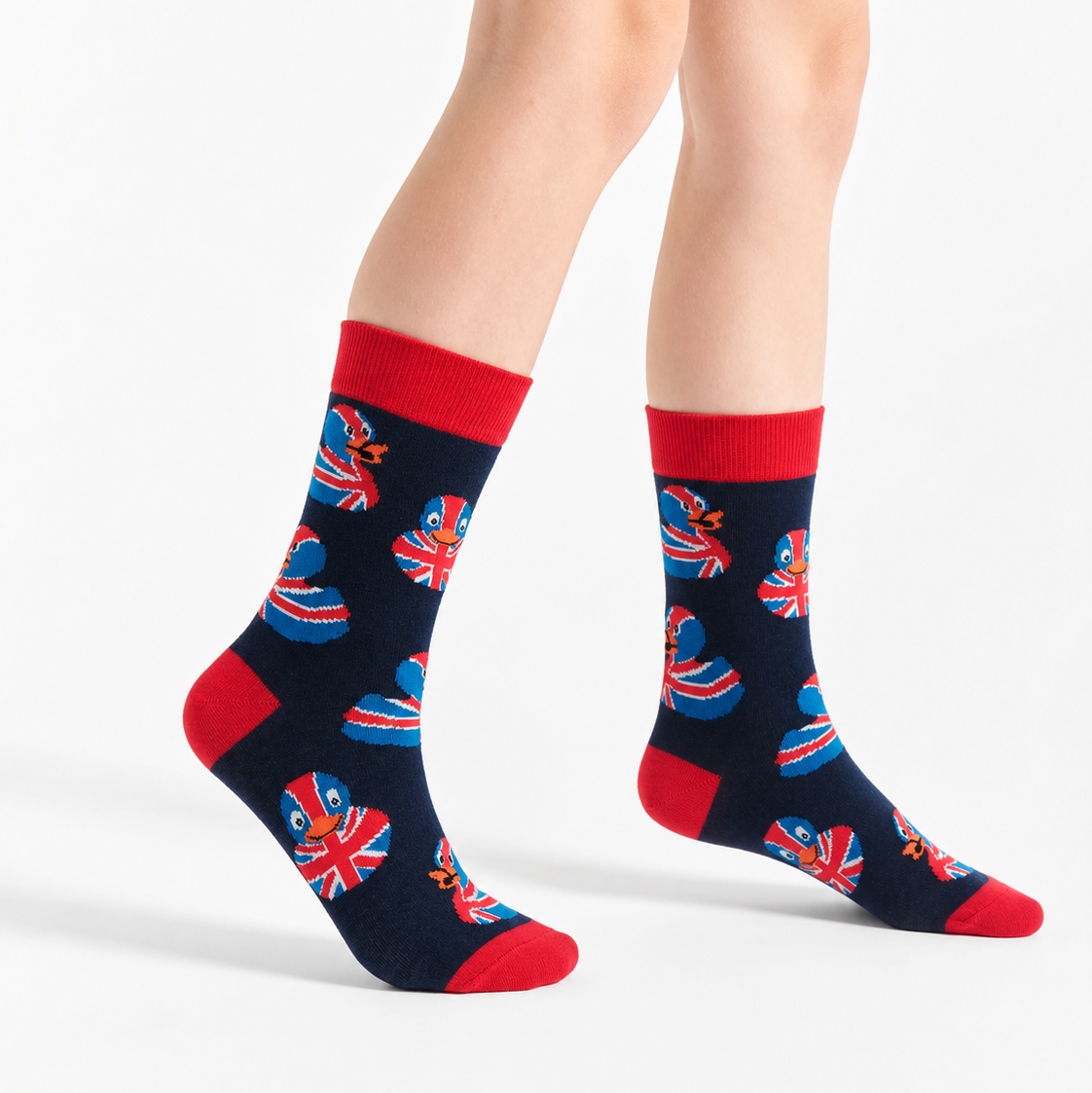 A pair of navy blue crew socks with red cuffs, heels, and toes, featuring a repeating pattern of red, white, and blue heart-shaped Union Jack flags, shown on a model's feet against a light gray studio background.