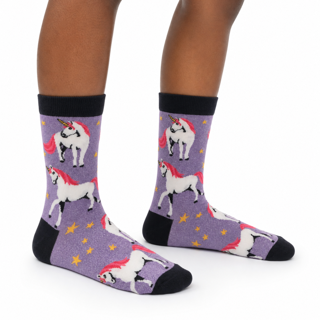A pair of crew socks with a purple background featuring a repeating pattern of white unicorns with red manesles and yellow stars, worn on a person's feet against a white background.